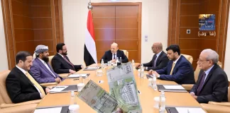 صورة لنصفين من عملة الريال اليمني فئة 1000 ريال، إحداها تتبع البنك المركزي في عدن وتحمل شعاره والأخرى تحمل شعار البنك المركزي في صنعاء ومتداولة في مناطق سيطرته، مع خلفية لإجتماع مجلس القيادة الرئاسي في عدن.