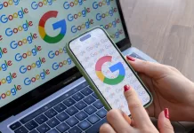 A woman looks at a mobile phone displaying the logo of Google in front of a laptop screen displaying the logo of Google.