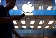 A pedestrian uses a smartphone while walking past an Apple store and logo in Hong Kong.