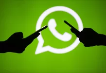 People hold mobile phones in front of the logo of WhatsApp application.