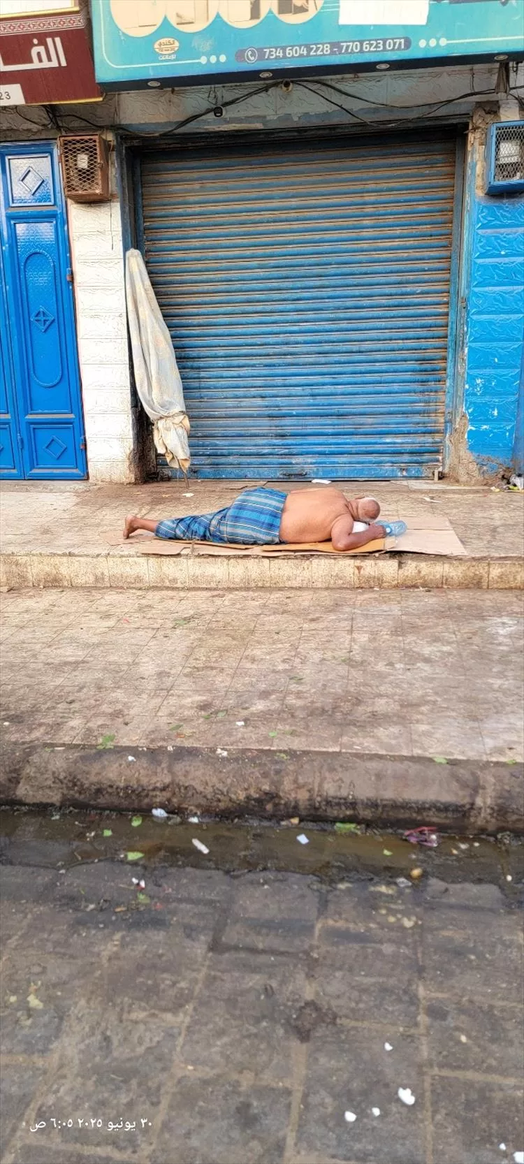صورة موجعة تختصر المعاناة.. مواطن يفترش رصيف الشارع في عدن هربًا من لهيب الحر وانقطاع الكهرباء