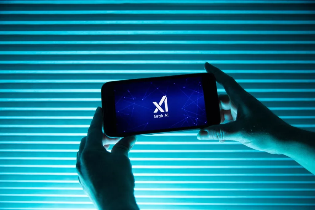A person holds a telephone displaying the logo of Elon Musk s artificial intelligence grok in front of a background lit by a blue light.