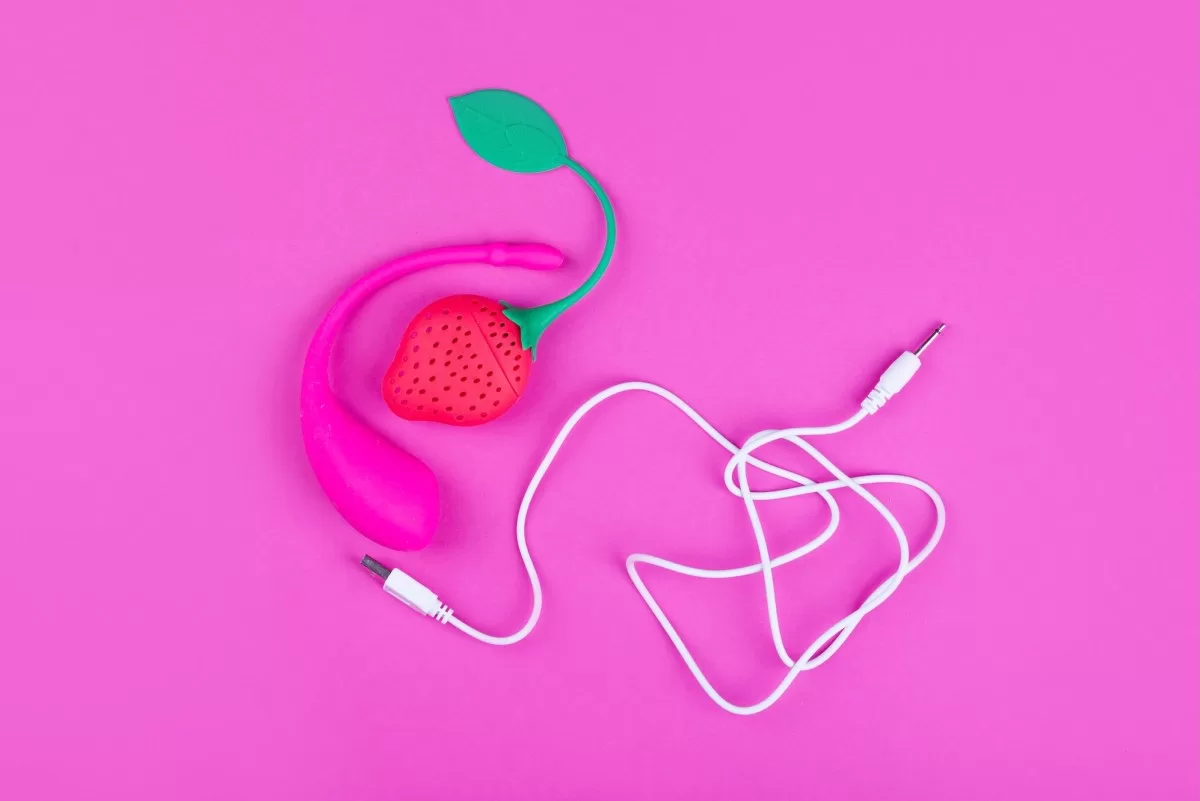 a photo of a female sex toy on a pink background, with a USB cable in the same shot