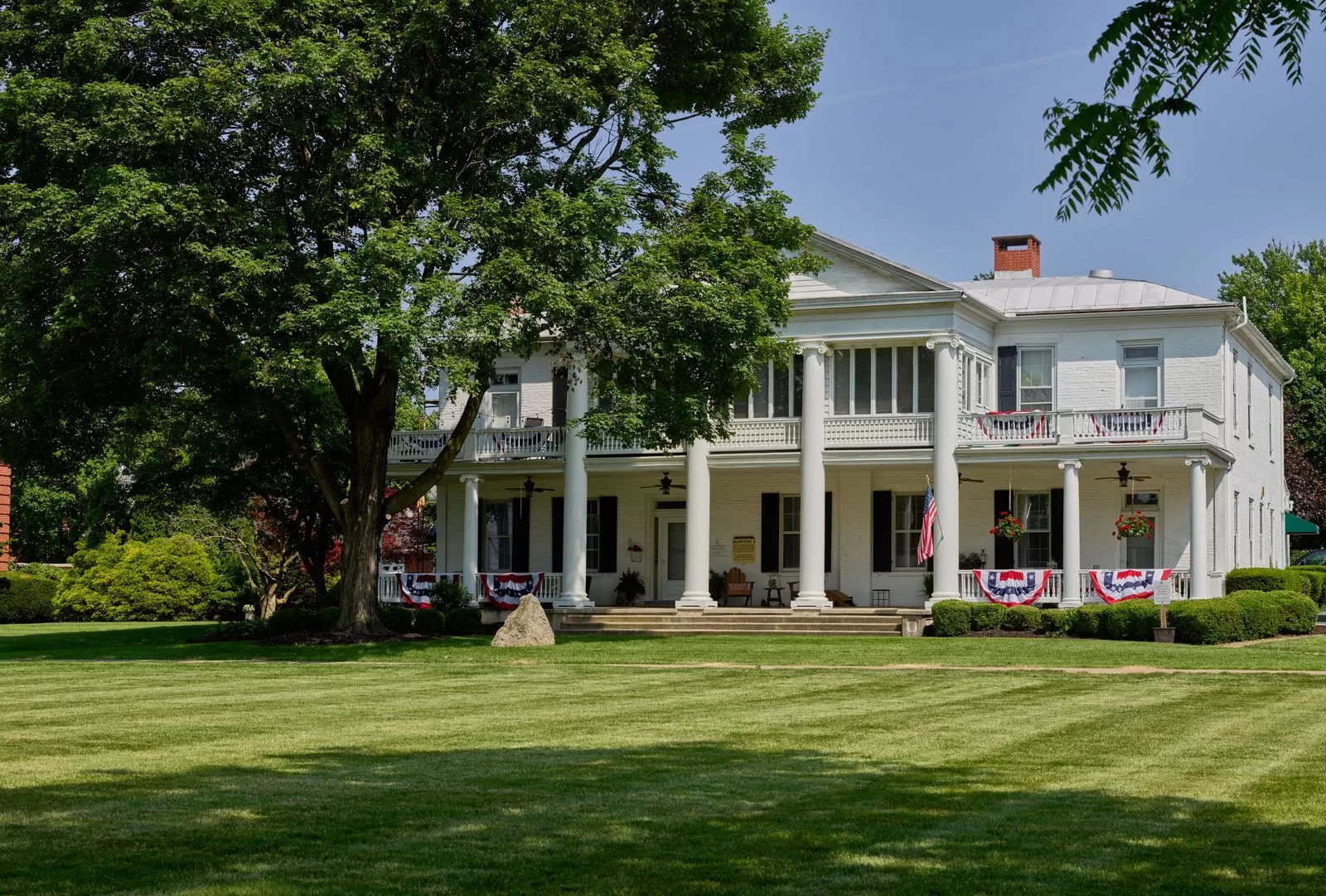 مبنى أبيض على عشب أخضر مرتب مع رواق وأعلام حمراء وبيضاء وزرقاء معلقة على الدرابزين