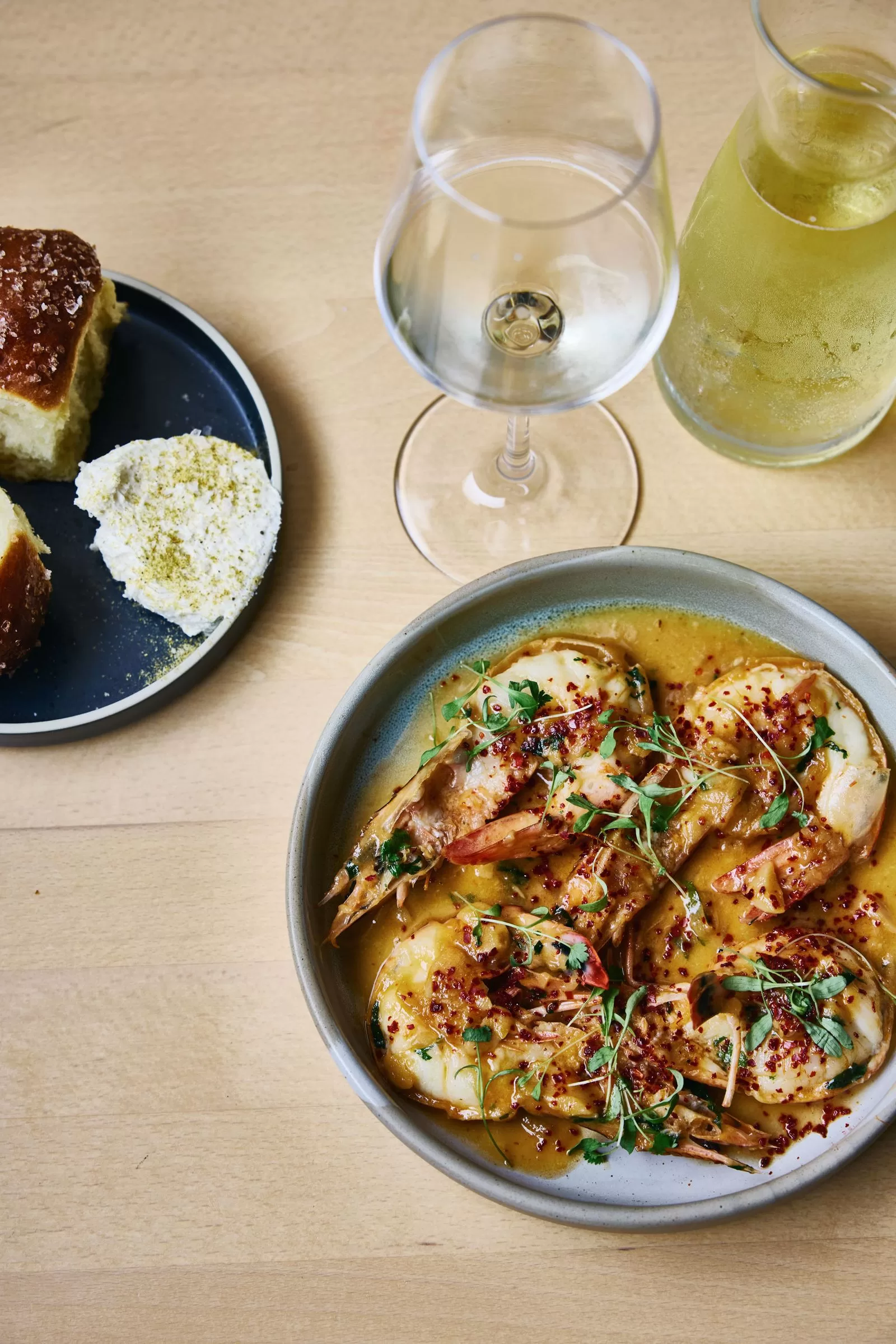 صورة لطبق من الجمبري مع جانب من الخبز وكأس من العصائر الأبيض على سطح خشبي