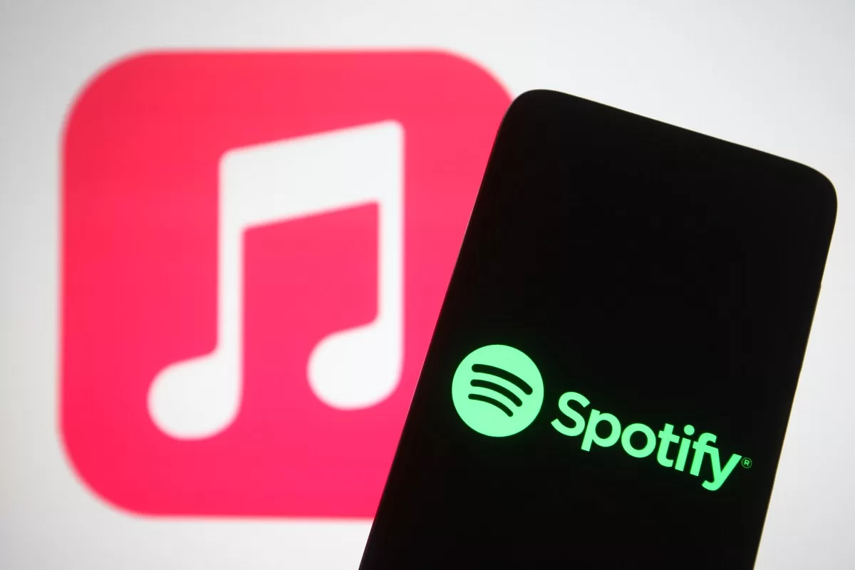 The Spotify logo seen displayed on a smartphone screen in front of Apple Music logo in the background.