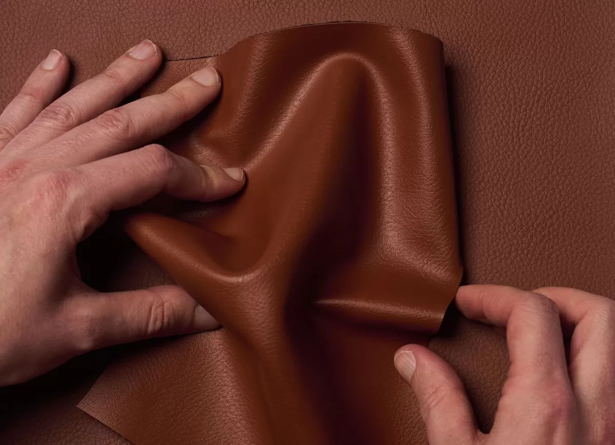 Two hands crumple Uncaged Innovations' artificial leather.
