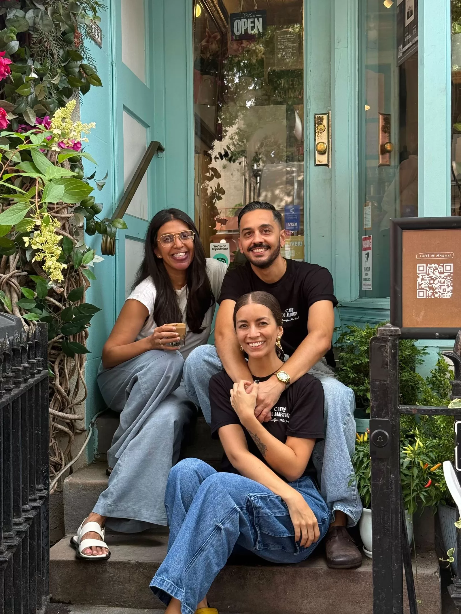 ثلاثة أشخاص يجلسون على درجات مدخل مقهى مبتسمين