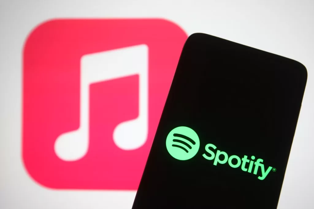 The Spotify logo seen displayed on a smartphone screen in front of Apple Music logo in the background.