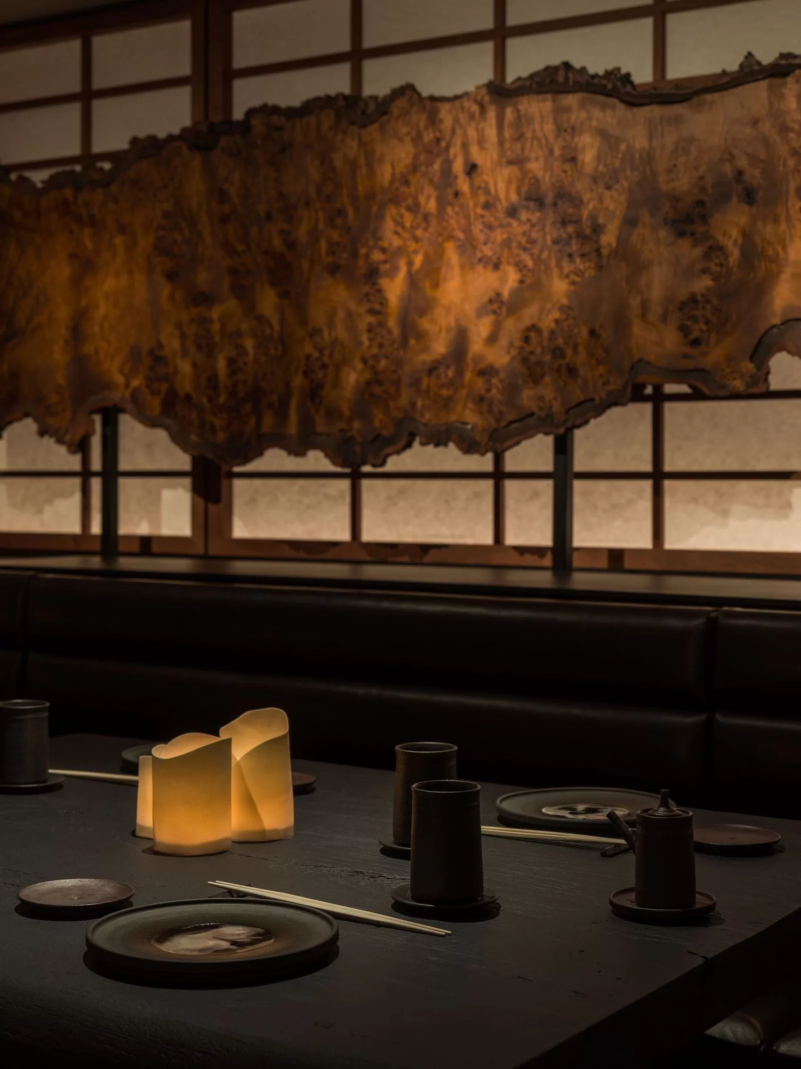 إعداد الطاولة مع أواني الطعام الداكنة ومفرش الطاولة وجدار فاصل من الورق والخشب في الخلفية