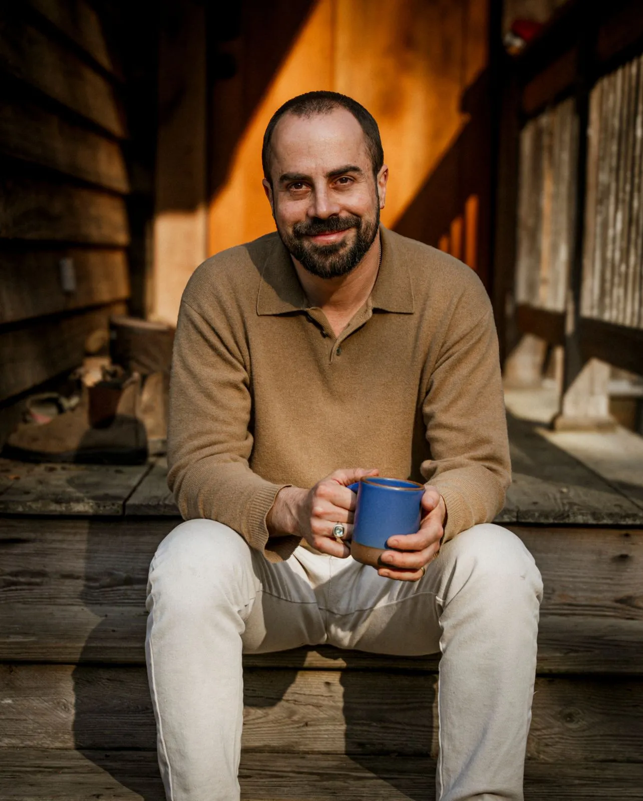 الصورة قد تحتوي على شخص جالس وكوب ووجه بالغ وابتسامة وملابس وسروال