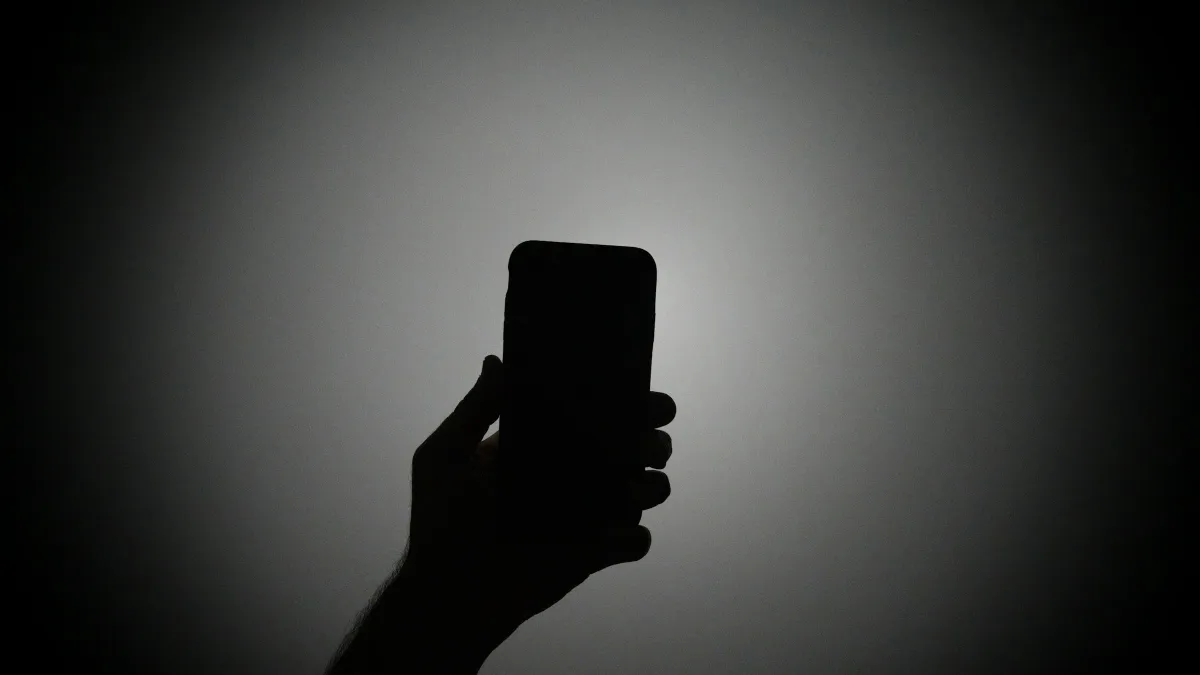 The silhouette of a hand holding an iPhone with the light on.