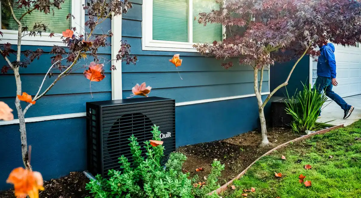 A dark grey heat pump sits outside a blue home.