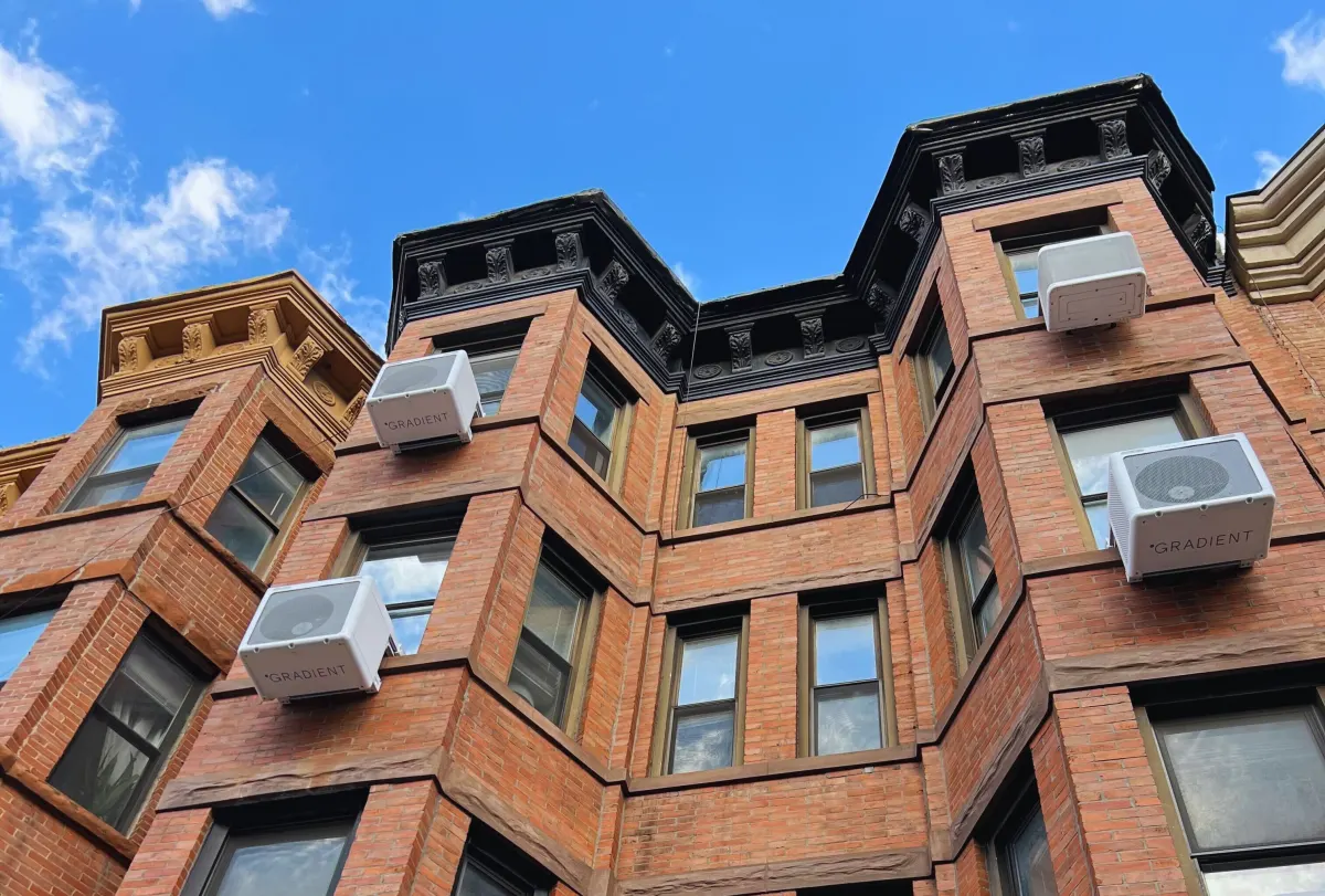 Heat pumps hang on the outside of an apartment building.