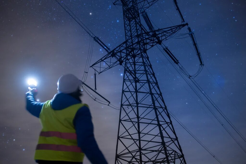 High-voltage engineer working on power lines at night.