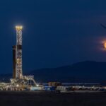 Fervo's drilling rig lit up at night with the moon rising in the background.